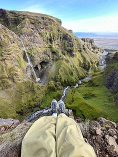 someone's feet resting on the edge of a cliff with a waterfall in the background