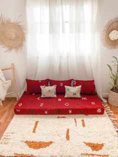 a red couch sitting in front of a window next to a white rug on top of a hard wood floor