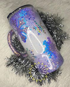 a purple and blue coffee mug sitting on top of a white fur covered floor next to tinsel