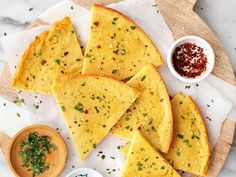 several pieces of flat bread on a wooden platter with dipping sauces next to it