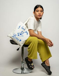 a woman sitting on top of a stool holding a tote bag