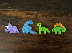 three different colored dinosaurs made out of perler beads on a wooden table with the word dino spelled in small letters