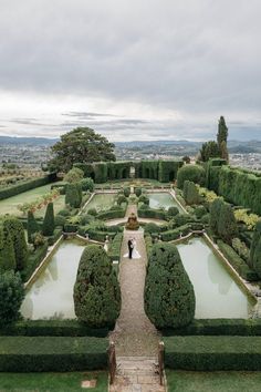 a bride and groom standing in the middle of a formal garden with hedges, water and trees