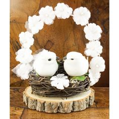 two white birds sitting in a nest on top of a piece of driftwood with flowers around it