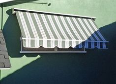 an awning on the side of a green building next to a window with blue shutters