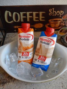 two bottles of protein drink sitting on top of ice in front of a coffee shop sign