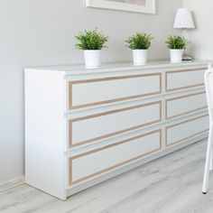 three potted plants sit on top of a white dresser next to a chair and lamp