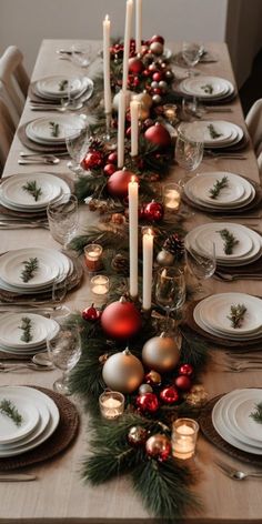 a dining table set for christmas dinner with candles and ornaments on the centerpieces