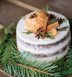 a cake decorated with oranges and cinnamon sticks on top of pine needles, surrounded by greenery