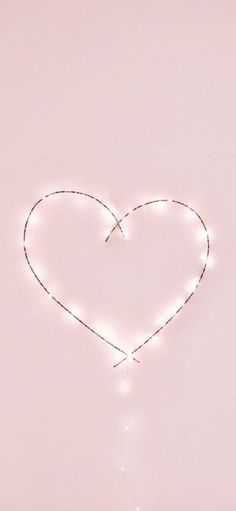 a heart - shaped string light hanging from the side of a wall in front of a pink background