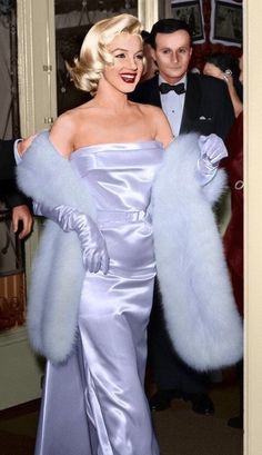 a woman in a silver dress and fur stole around her shoulders with a man in a tuxedo standing behind her