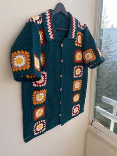 a crocheted sweater hanging on a wall next to a window