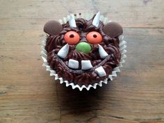 a cupcake with chocolate frosting and decorations on it's face is sitting on a wooden table