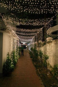 a man walking down a walkway covered in white lights and greenery on both sides