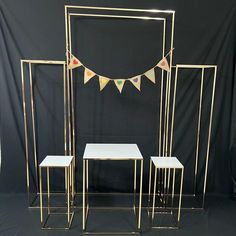 three tables and two stools are in front of a black backdrop with bunting flags