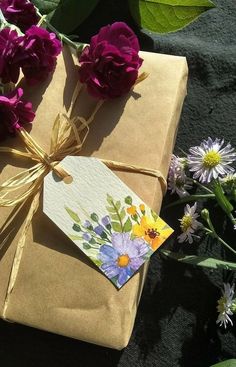 a gift wrapped in brown paper and tied with a yellow ribbon next to purple flowers