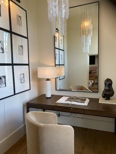 a desk with a mirror, chair and lamp on it in front of pictures hanging on the wall