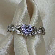 a fancy ring with a heart shaped center surrounded by diamonds on a white satin background