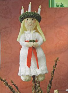 the knitted doll is wearing a white dress and holding a red ribbon in her hands