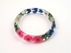 "This lightweight Slip on Bangle is made with Real Dried bright pink and white daisies, Texas bluebonnet and green leaves embedded into crystal clear resin and shaped into a unique and stylish bangle with Glassy finish that sparkles in the light. It is a chunky bangle with a curved profile; thicker in the center and tapering on the sides. This stunning bangle embodies contemporary resin jewelry for the nature lover. Bracelet measures: Inside diameter 2 3/4\" (69mm) high 5/8\" (16mm ) thick 11/64 Adjustable Resin Jewelry With Pressed Flowers, Multicolor Flower Jewelry With Pressed Flowers, Adjustable Bracelets With Pressed Flowers, Multicolor Flower Shaped Jewelry With Pressed Flowers, Adjustable Round Bracelets With Pressed Flowers, Spring Flower Shaped Jewelry With Pressed Flowers, Spring Flower Jewelry With Pressed Flowers, Adjustable Flower Bracelets With Pressed Flowers, Adjustable Pink Jewelry With Pressed Flowers