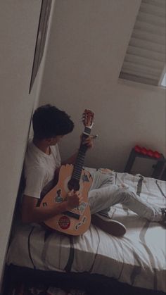 a man sitting on top of a bed with a guitar in his hand while holding it