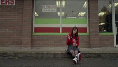 a woman sitting on the curb in front of a building talking on her cell phone