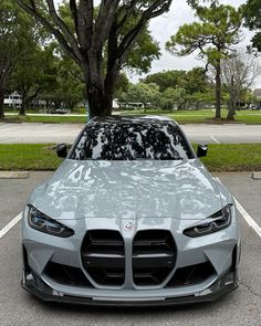 the front end of a silver sports car parked in a parking lot next to trees