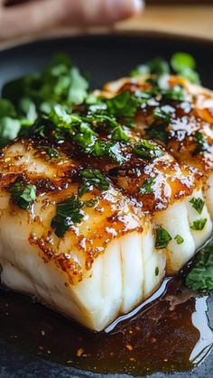 two fish fillets on a black plate with sauce and green garnishes