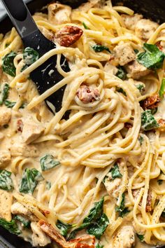 a skillet filled with pasta and spinach topped with chicken, cheese and sauce