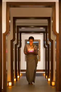 a man holding a lit candle in his hand while walking down a hallway with candles on either side