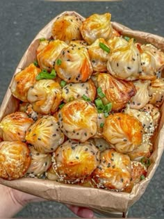 a person holding up a cardboard box filled with dumplings covered in sauce and sesame seeds