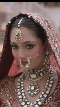 a woman in a red and gold outfit with jewelry on her head, wearing an elaborate necklace