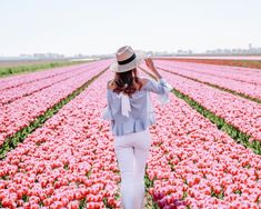 a woman standing in a field of tulips with a hat on her head