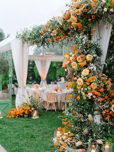 an outdoor wedding setup with orange flowers and greenery on the side of the aisle