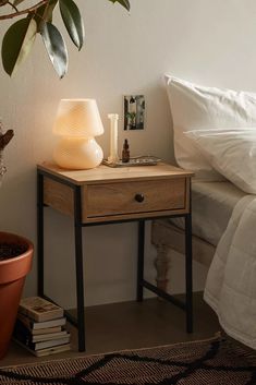 a nightstand with a lamp on top of it next to a bed and a potted plant