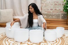 a woman sitting on the floor surrounded by white cups