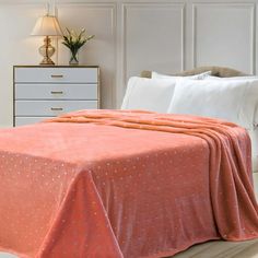 a bed with an orange bedspread on top of it and a white dresser in the background