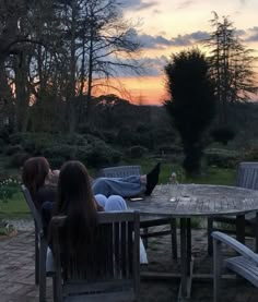 three people sitting at a table with drinks in front of the sun setting behind them