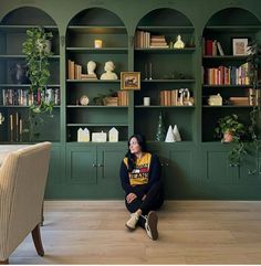 a woman sitting on the floor in front of green bookshelves with shelves full of books