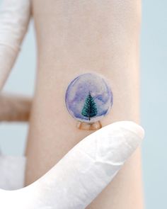 a person with a snow globe tattoo on their left arm and the image of a pine tree in it