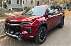 a red chevrolet suv is parked on the side of the road in front of a house