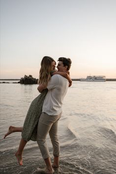 a man and woman are hugging on the beach by the water at sunset, with a cruise ship in the background