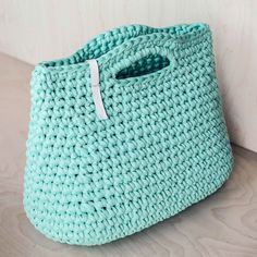 a blue crocheted bag sitting on top of a wooden table next to a white wall