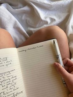 a person writing on a notebook with a pen in their hand while laying down next to a bed