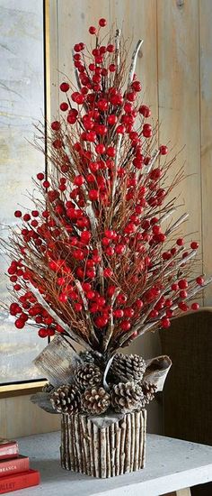 a vase with red berries and pine cones in it on a table next to books