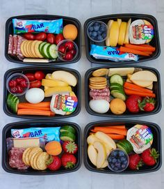 four plastic trays filled with different types of fruit and veggies, along with snacks