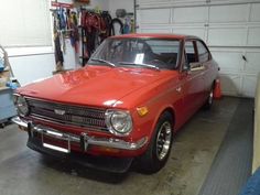 an old red car parked in a garage next to a wall with tools hanging on it