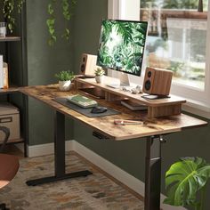 a desk with a computer on it in front of a window and bookshelf