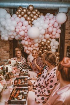 three women sitting at a table surrounded by balloons and confetti in front of them