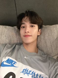 a young man laying on top of a couch wearing a nike shirt and looking at the camera